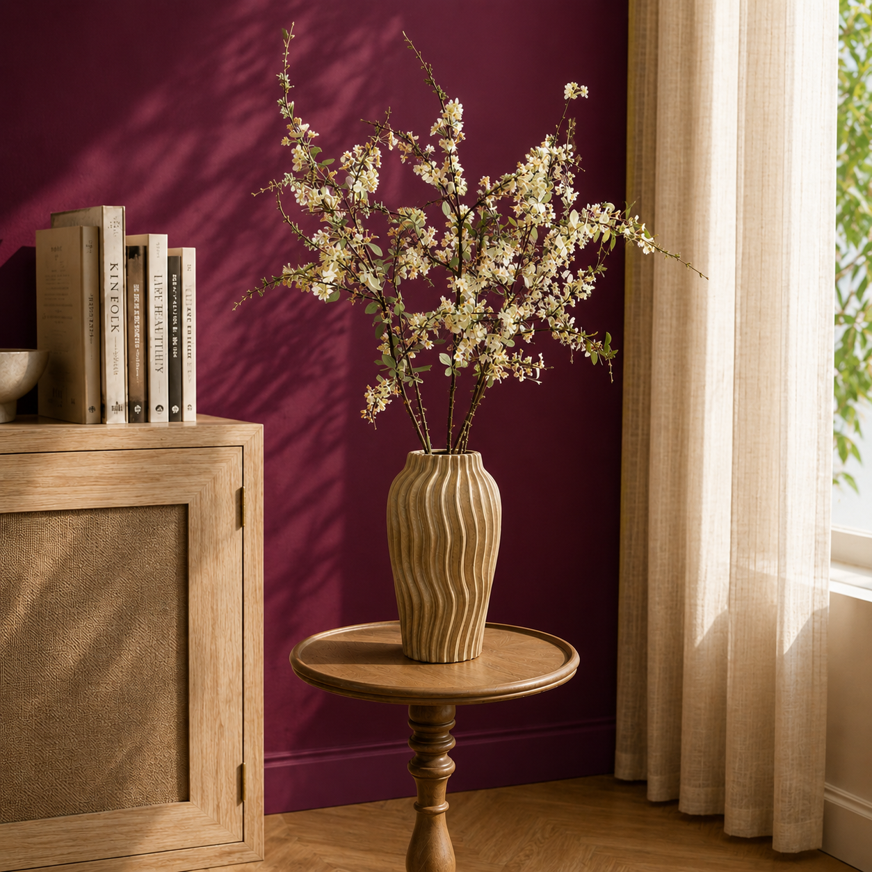 Vase with flowers on a wooden table against a purple wall with books stacked on a wooden cabinet.